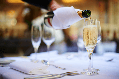 Eine Person gießt Champagner in ein Glas an einem gedeckten Tisch.
