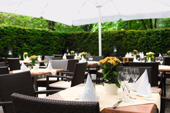 Ein Außenbereich mit Tischen und Stühlen, gedeckt mit Gläsern, Servietten und Blumenarrangements,…