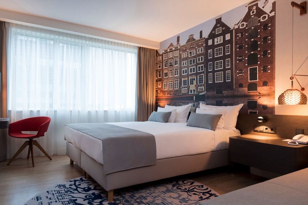 Um quarto de hotel moderno com uma cama, mesas de cabeceira, uma cadeira e uma grande janela com…