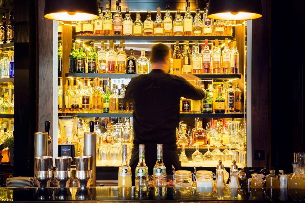 A bartender is arranging bottles on shelves behind a bar counter.