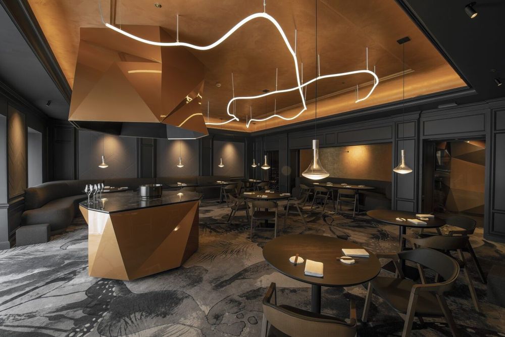 The photo shows a modern, stylish interior of a dining or lounge area with multiple tables,…