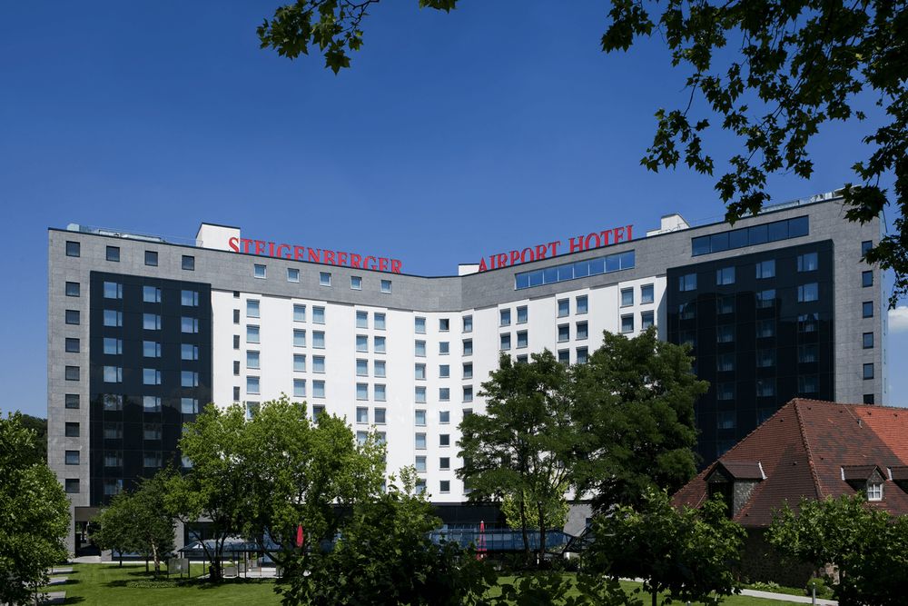 The photo shows a large hotel building with the words "Steigenberger Airport Hotel" on top,…