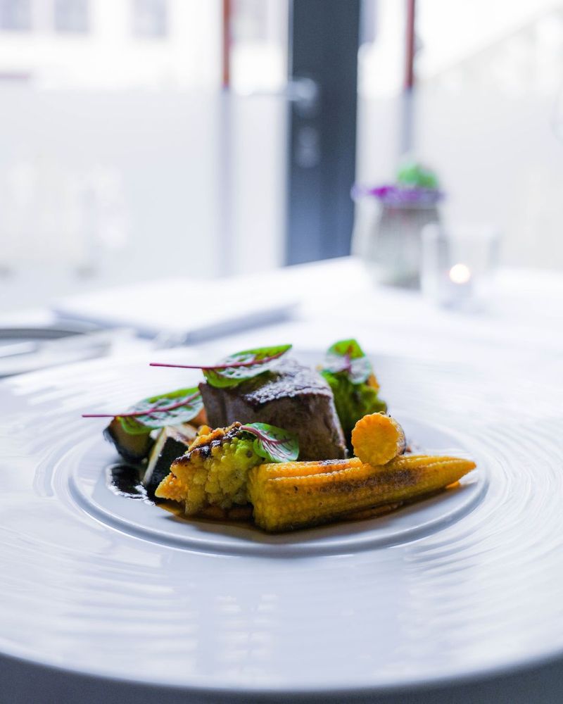 A gourmet dish with a piece of meat, baby corn, and vegetables on a white plate.
