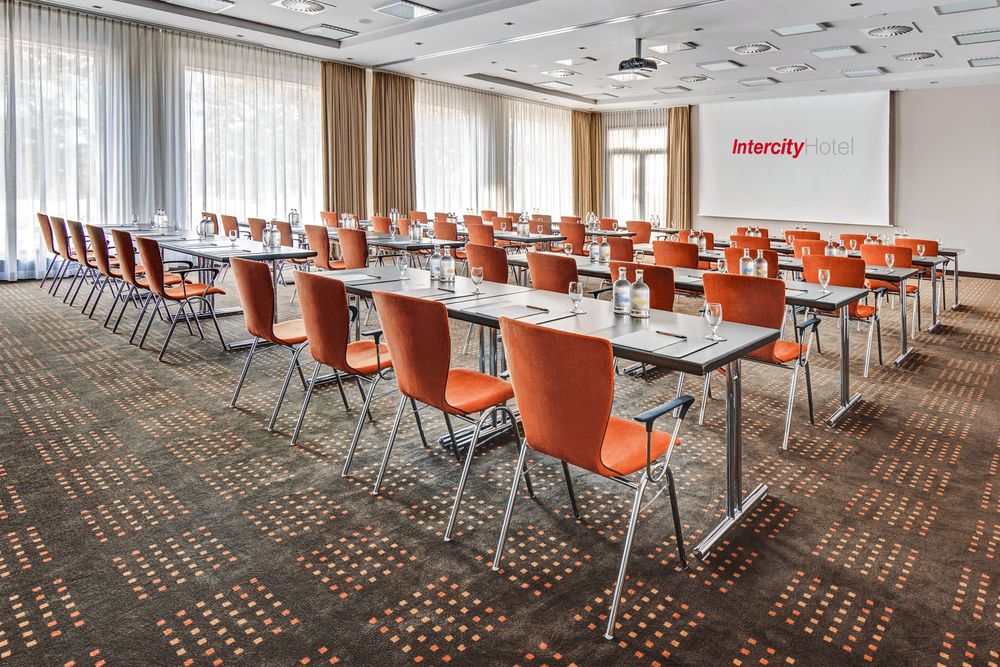 The photo shows a conference or meeting room with rows of tables and chairs arranged for an event.