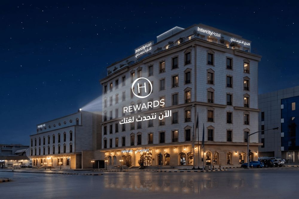 Das Foto zeigt ein großes, gut beleuchtetes Hotelgebäude bei Nacht mit beleuchteten Schildern und…