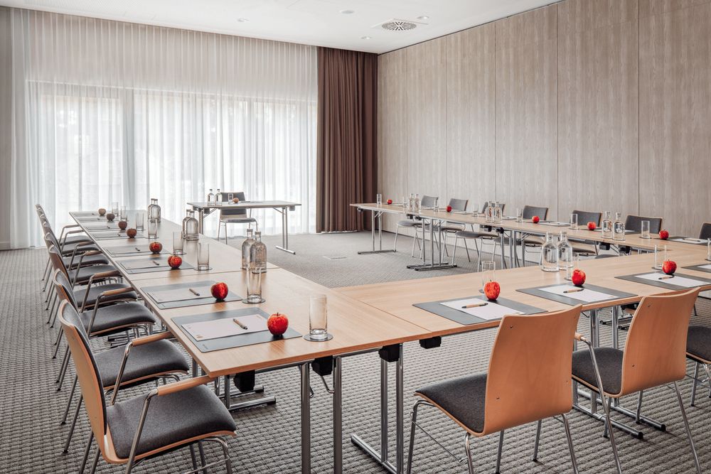 A conference room set up with tables and chairs arranged in a U-shape for a meeting or seminar.