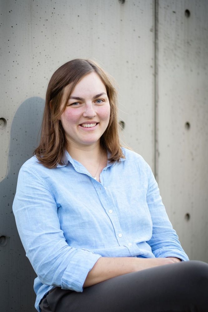 A woman sitting and smiling against a concrete wall.