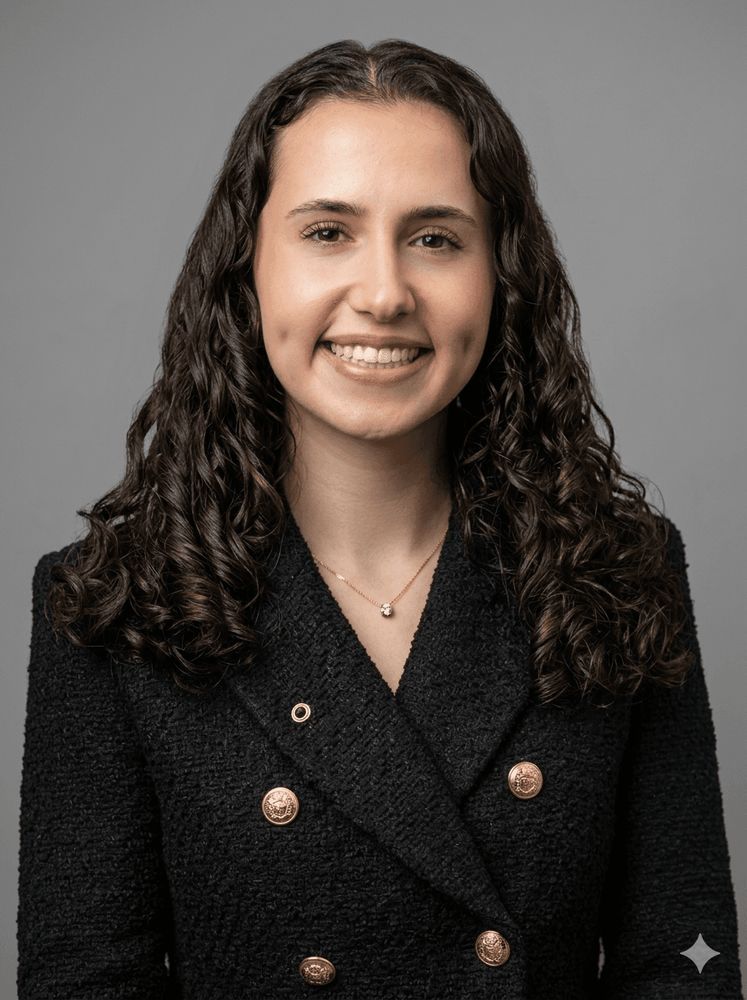 A portrait of a smiling woman with curly hair wearing a dark coat with gold buttons.
