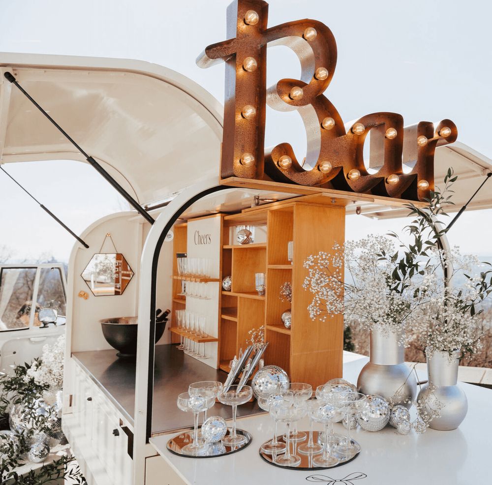 Ein kleiner Außenbarbereich mit einem beleuchteten "Bar"-Schild, Gläsern und dekorativen Blumen.