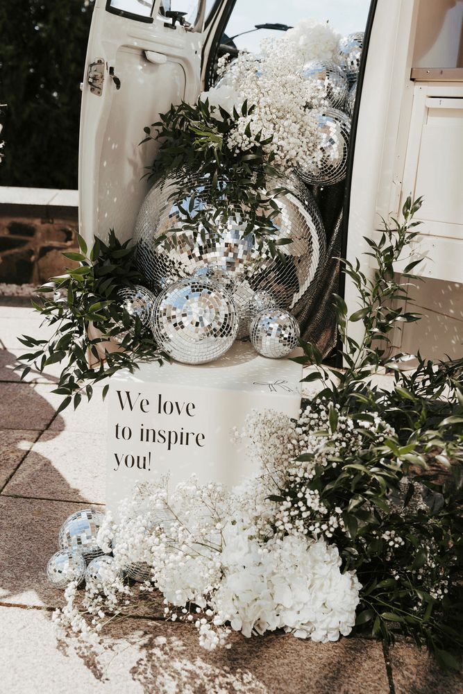 Das Foto zeigt eine dekorative Anordnung mit Diskokugeln, Grünpflanzen, weißen Blumen und einem…