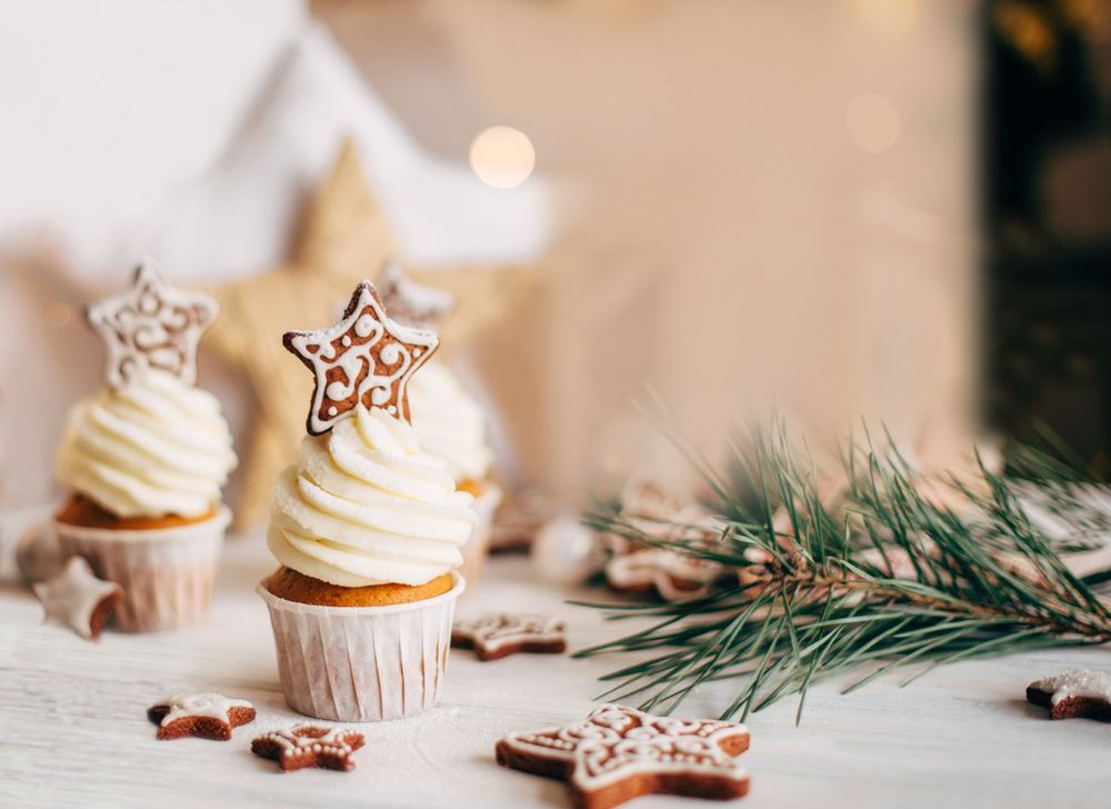 На фото показані кексики з білою глазур'ю, прикрашені печивом у формі зірок, поруч гілки сосни та…
