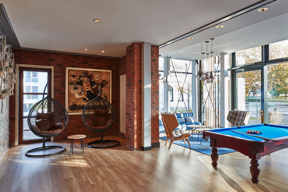 Das Foto zeigt einen modernen Lounge-Bereich mit Hängestühlen, einem Tisch, einem Billardtisch und…