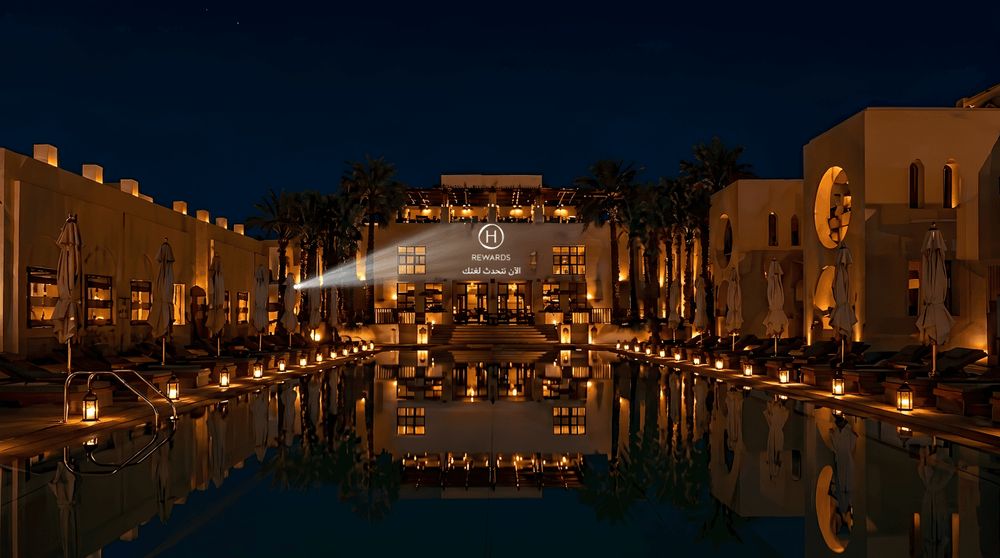 Eine nächtliche Ansicht eines gut beleuchteten, luxuriösen Gebäudes mit einem reflektierenden Pool…