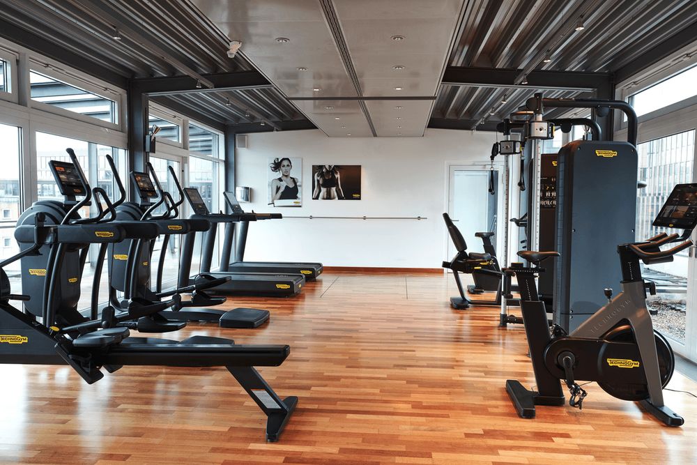Ein modernes Fitnessstudio mit Trainingsgeräten wie Laufbändern, Heimtrainern und Rudergeräten.