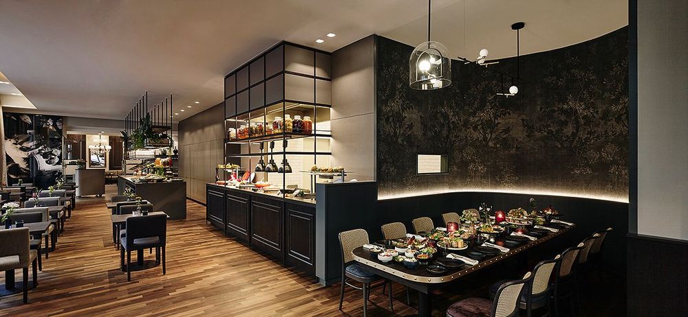 Das Foto zeigt das Innere eines modernen Restaurants mit Tischen, Stühlen und einem Buffetbereich.