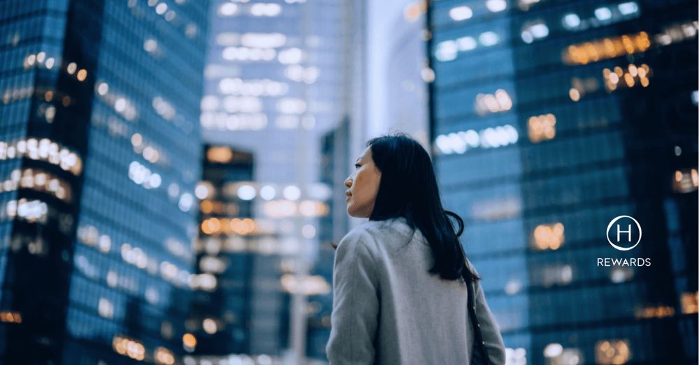 Eine Frau schaut sich nachts beleuchtete Wolkenkratzer in einer Stadt an.