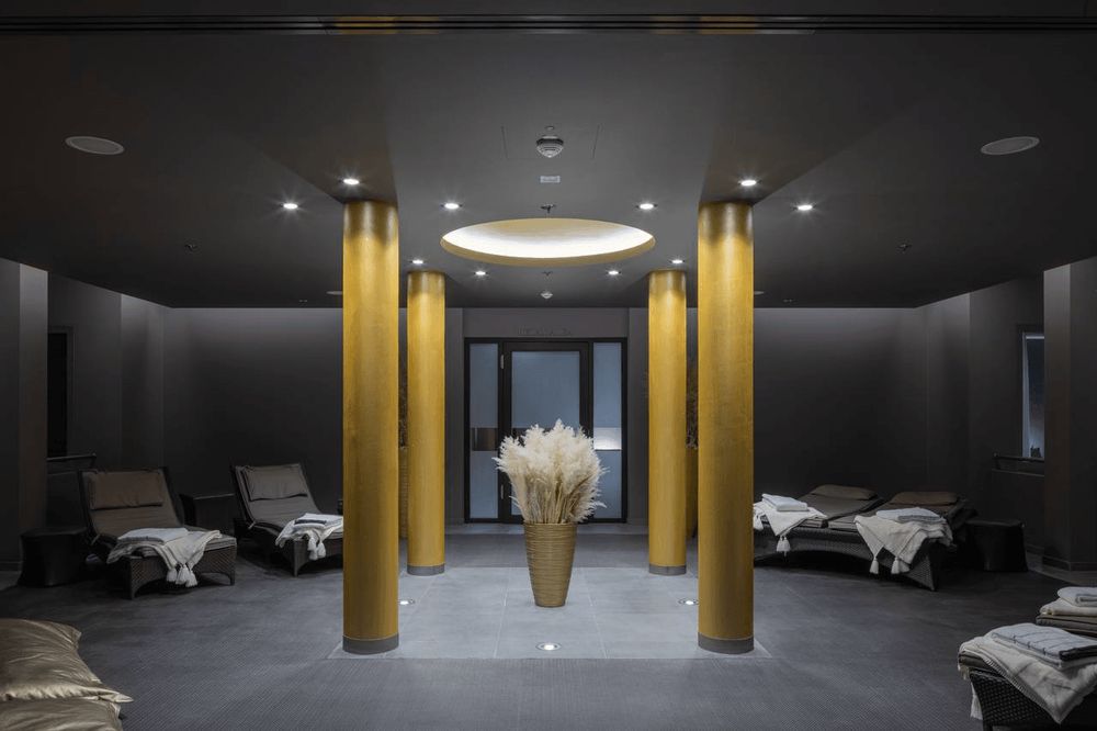 A modern, minimalistic interior space with lounge chairs, golden pillars, and a decorative…