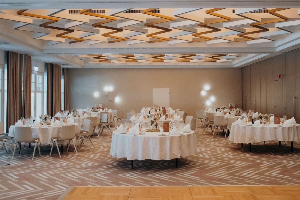 Une salle de banquet aménagée avec des tables rondes recouvertes de nappes blanches pour un…