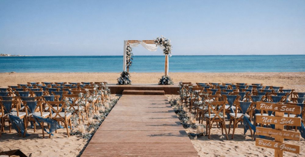 一个户外海滩婚礼布置，椅子排列在通向海边装饰拱门的过道两侧。