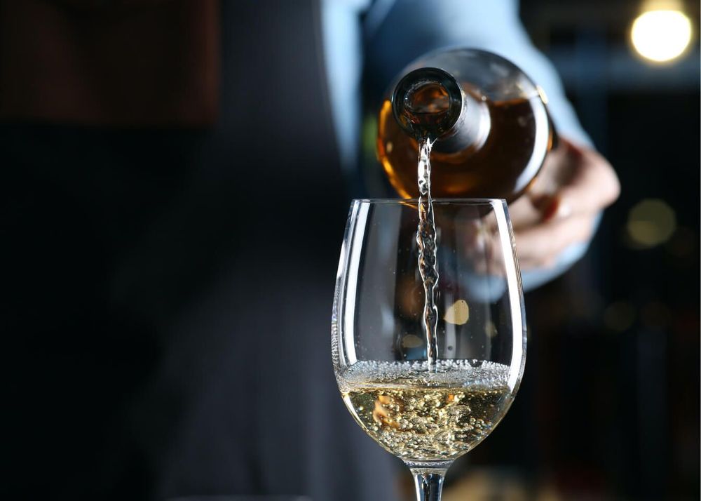 A person is pouring white wine into a glass.