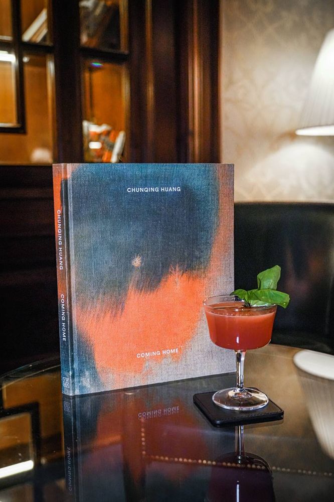 Un livre intitulé "Coming Home" de Chunqing Huang est posé sur une table à côté d'un verre de…