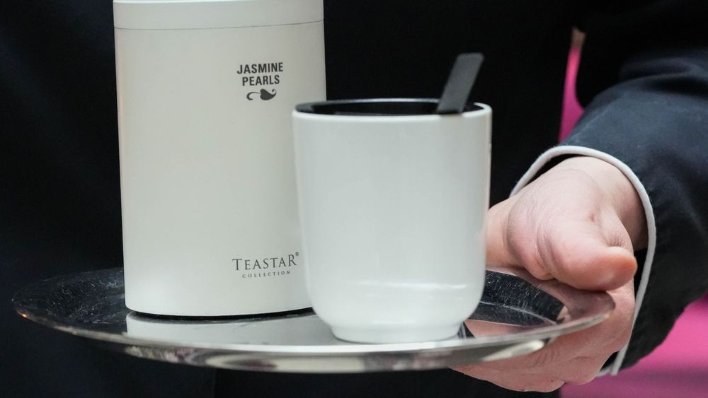 A person is holding a tray with a cup and a container labeled "Jasmine Pearls."