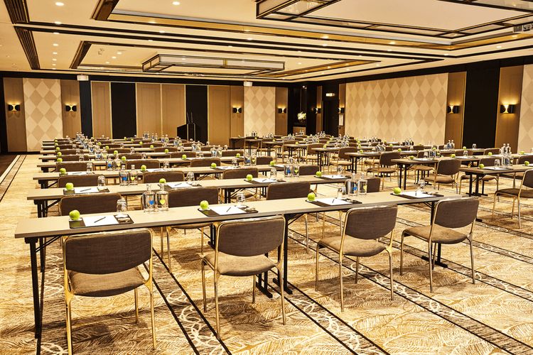 A conference room set up with multiple rows of tables and chairs, each table has water bottles, glasses, and green apples.