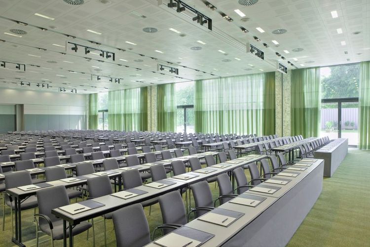 Ein großer Konferenzraum mit Reihen von Tischen und Stühlen, an jedem Tisch Notizblöcke und…