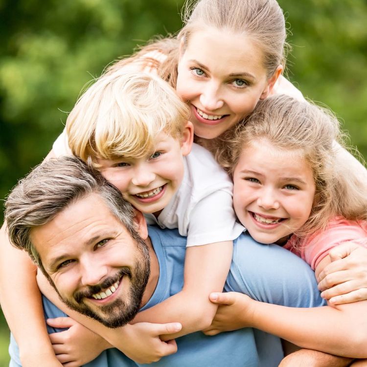 Das Foto zeigt eine glückliche vierköpfige Familie, die sich im Freien umarmt und lächelt.