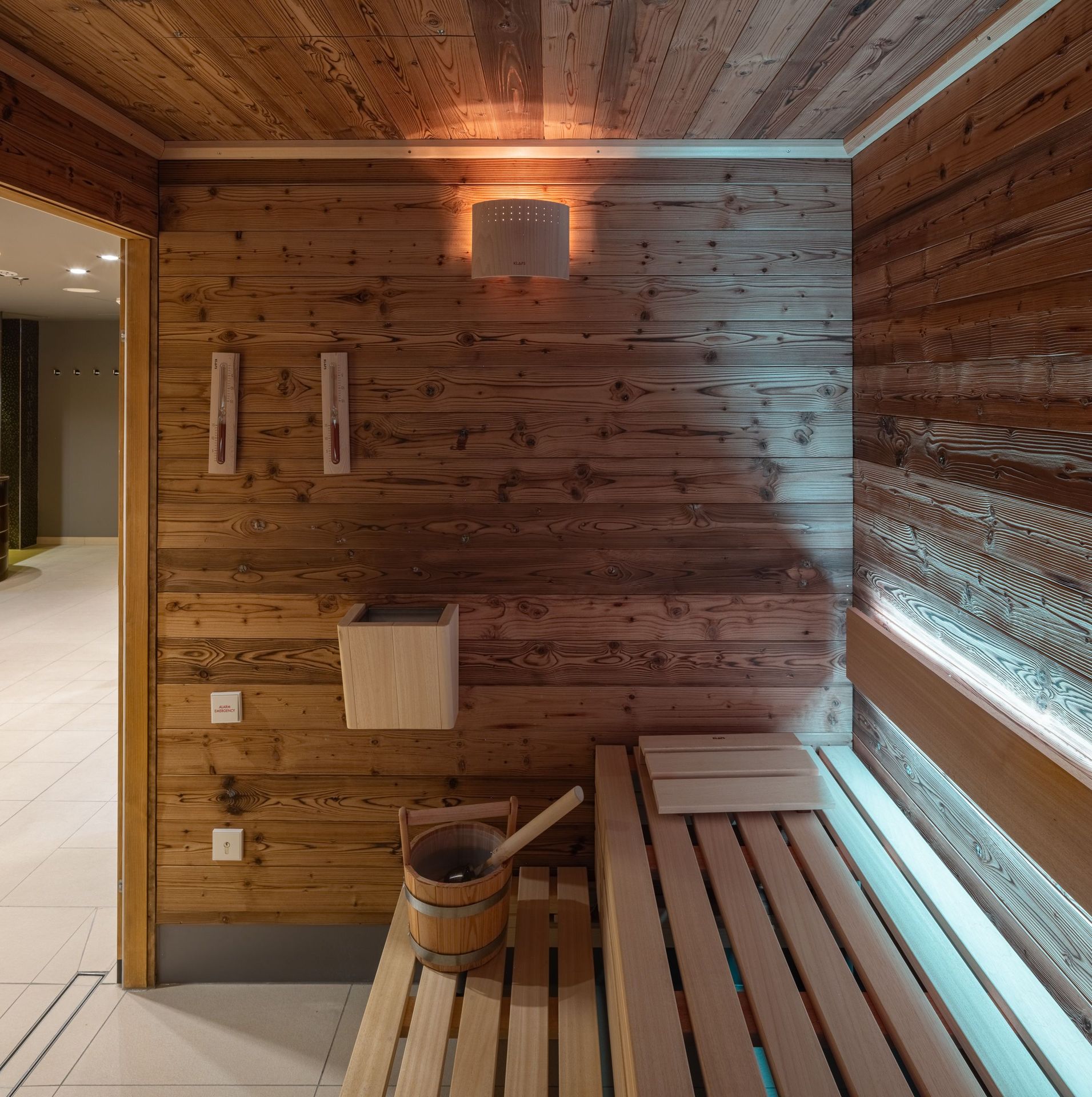 The photo shows a wooden sauna room with benches, a bucket, and a ladle.