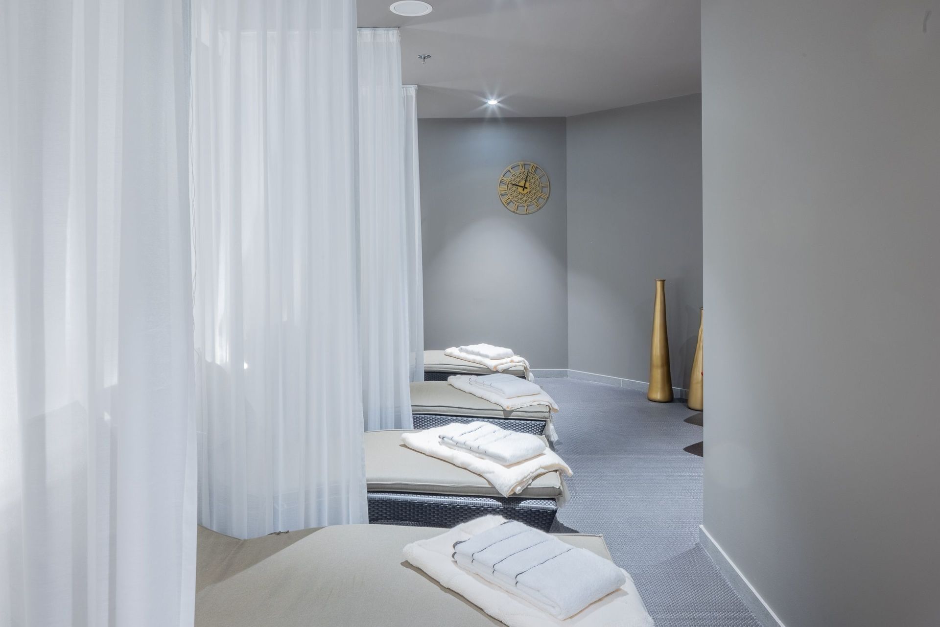 Ein Spa- oder Ruheraum mit Liegestühlen und gefalteten Handtüchern, getrennt durch weiße Vorhänge.