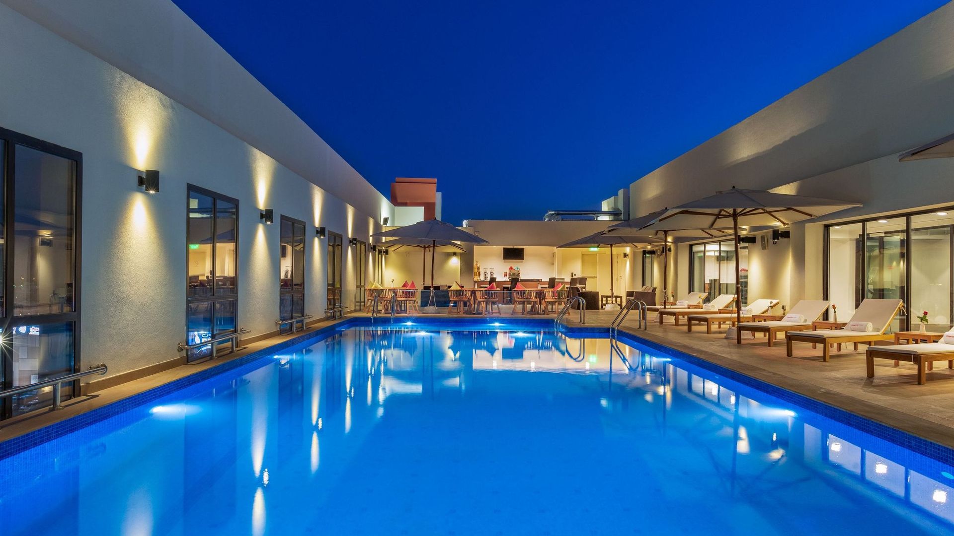 A modern outdoor swimming pool area at night with lounge chairs and umbrellas along the sides.