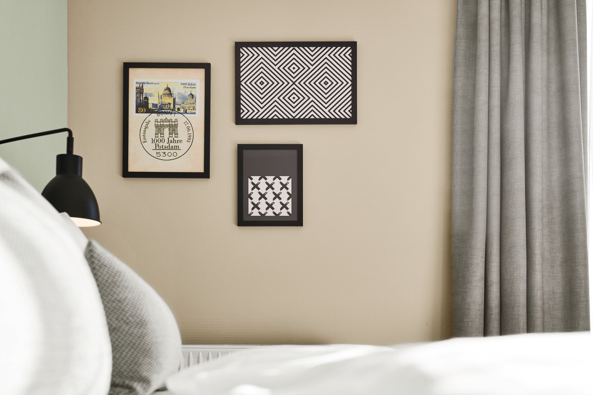 Una parete della camera da letto con tre opere d'arte incorniciate sopra un letto con cuscini e…