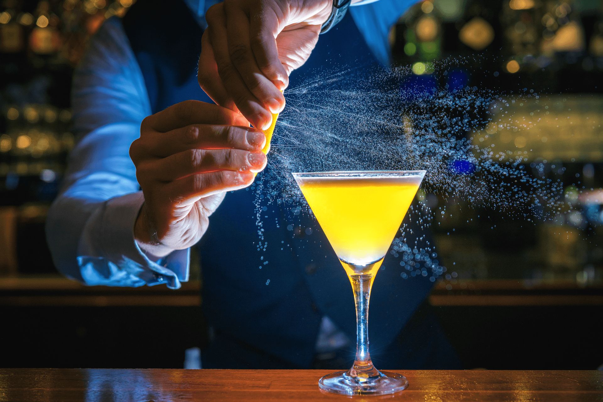 Ein Barkeeper bereitet einen Cocktail zu und sprüht oder reibt Zitronenschale über das Getränk in einem Martiniglas.