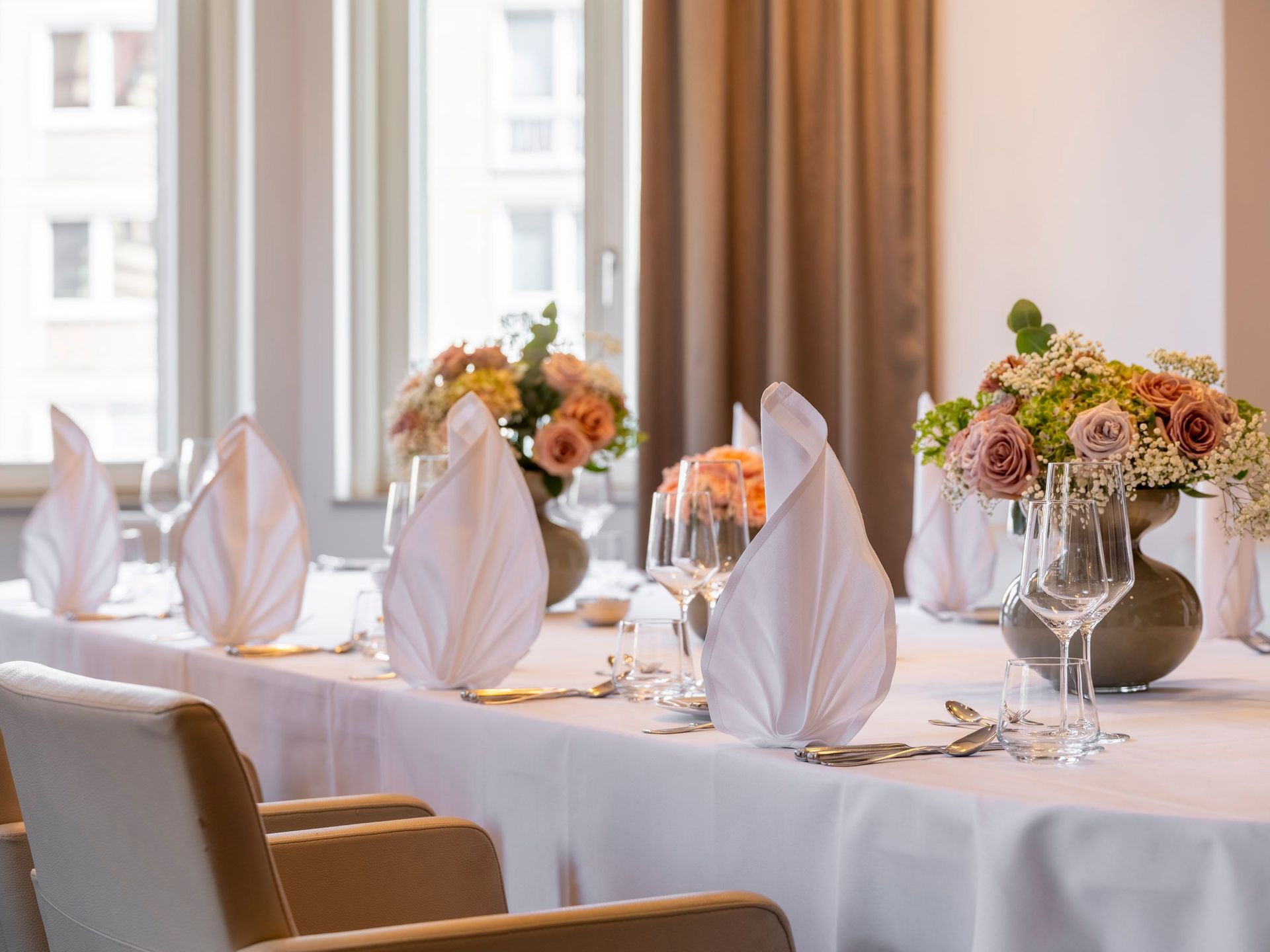 Ein Esstisch, elegant gedeckt mit gefalteten Servietten, Gläsern und Blumenarrangements.