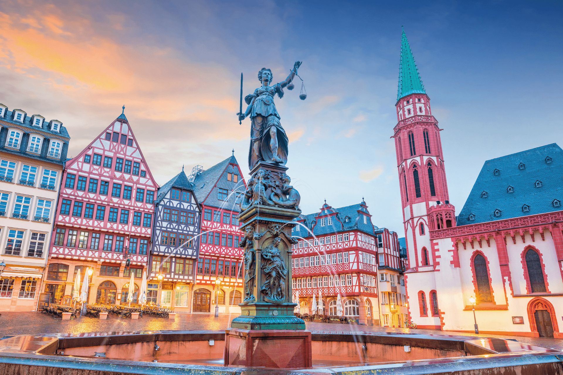 La foto mostra una piazza storica con edifici tradizionali in legno a vista europei, una chiesa…