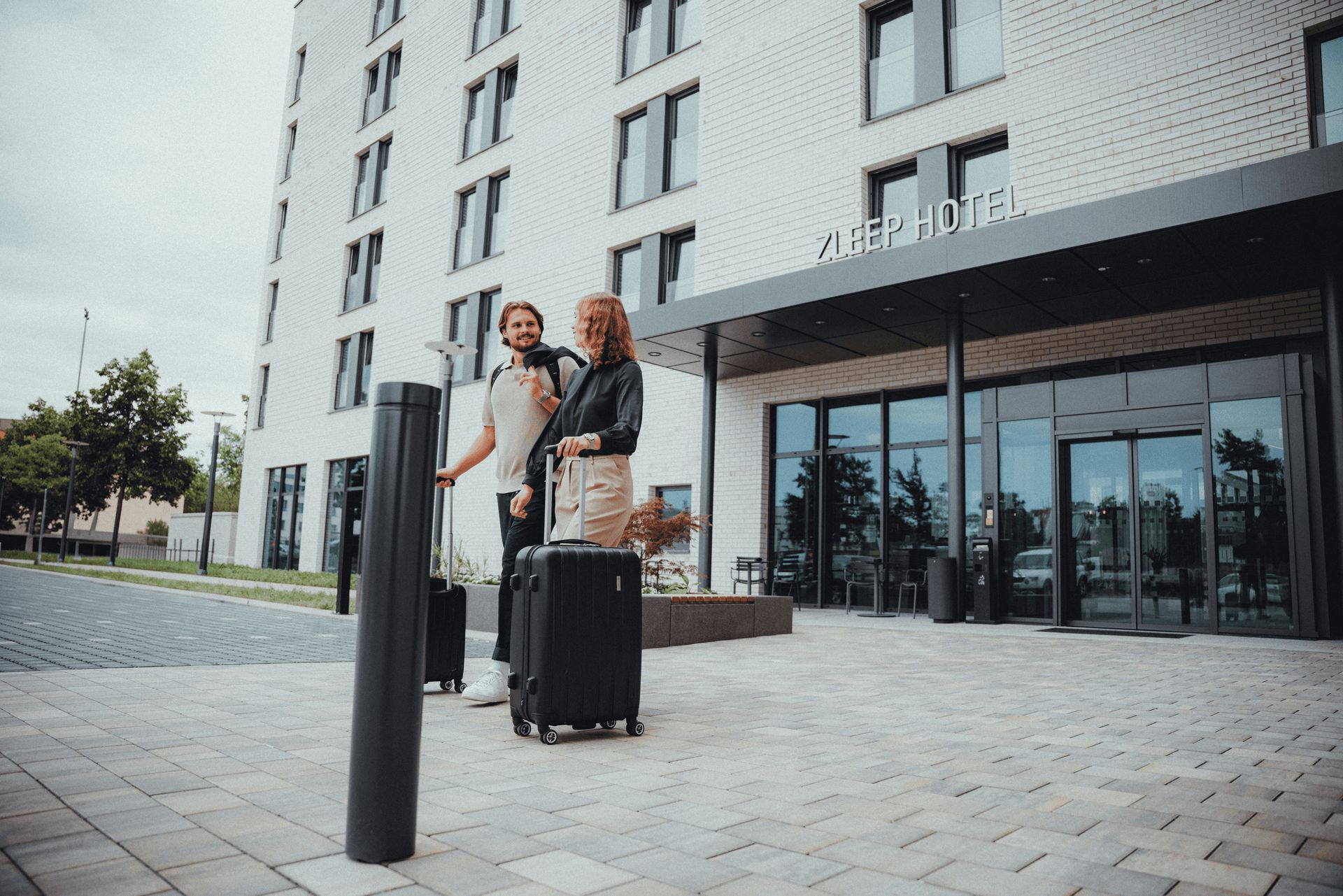 Two people with luggage standing outside a hotel entrance.