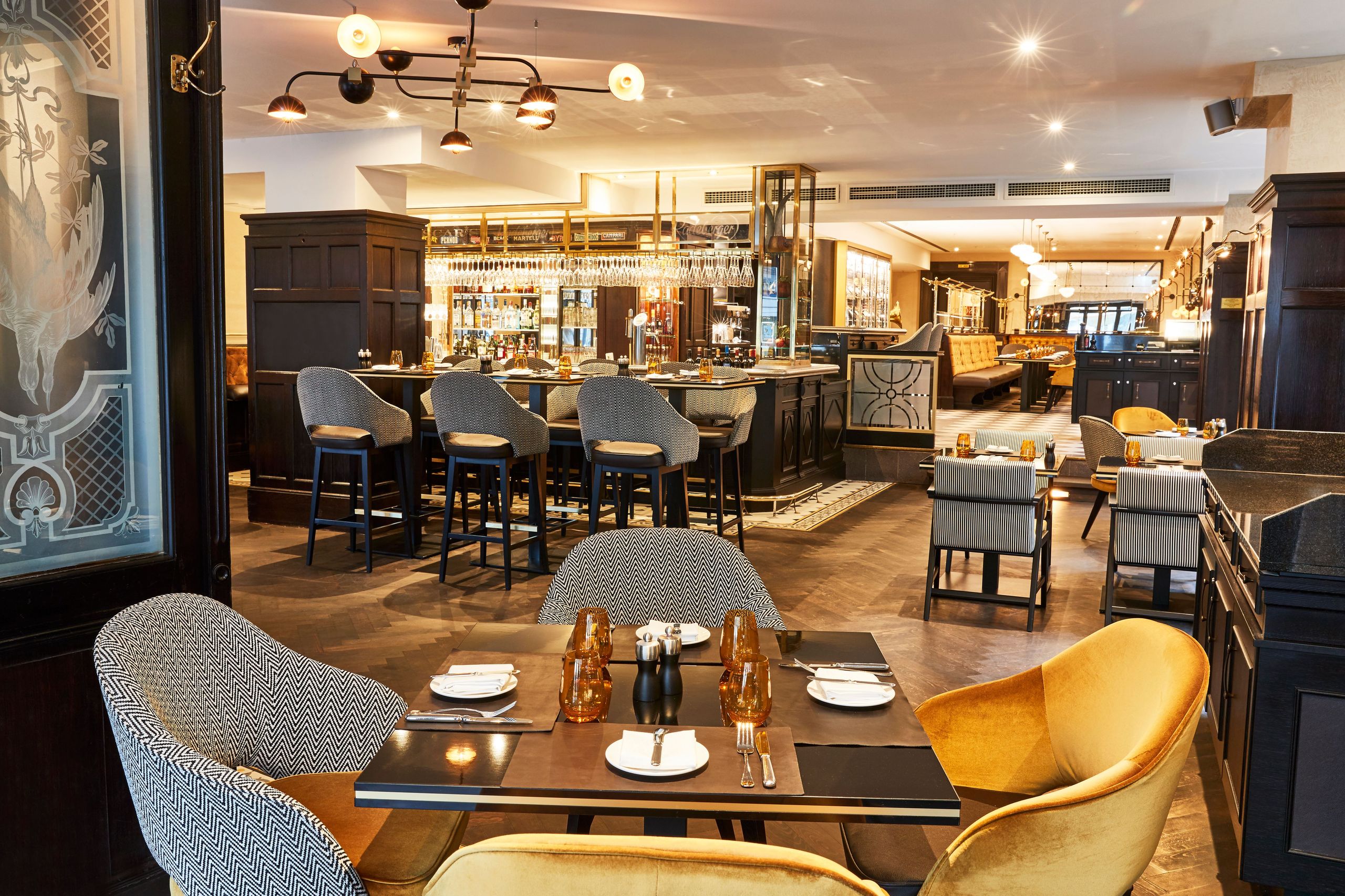 Fotot visar insidan av en modern, välmöblerad restaurang med bord, stolar och en bardel i…