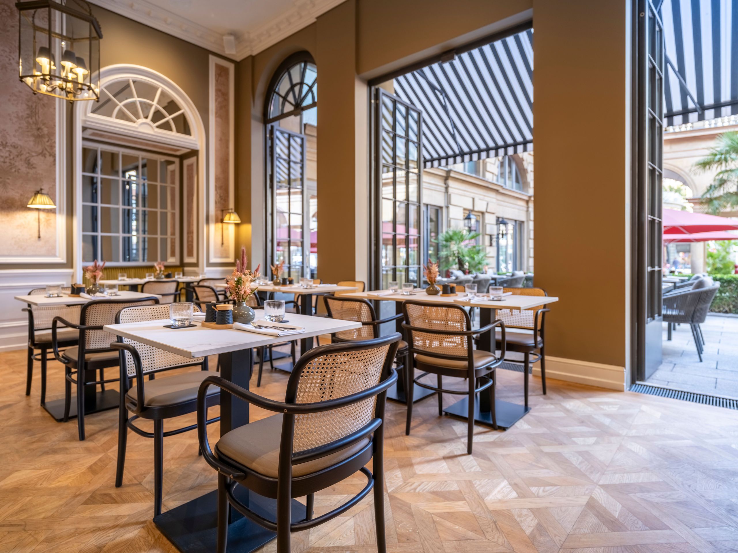 Das Foto zeigt einen eleganten Innen-Außen-Essbereich eines Restaurants oder Cafés mit Tischen und…