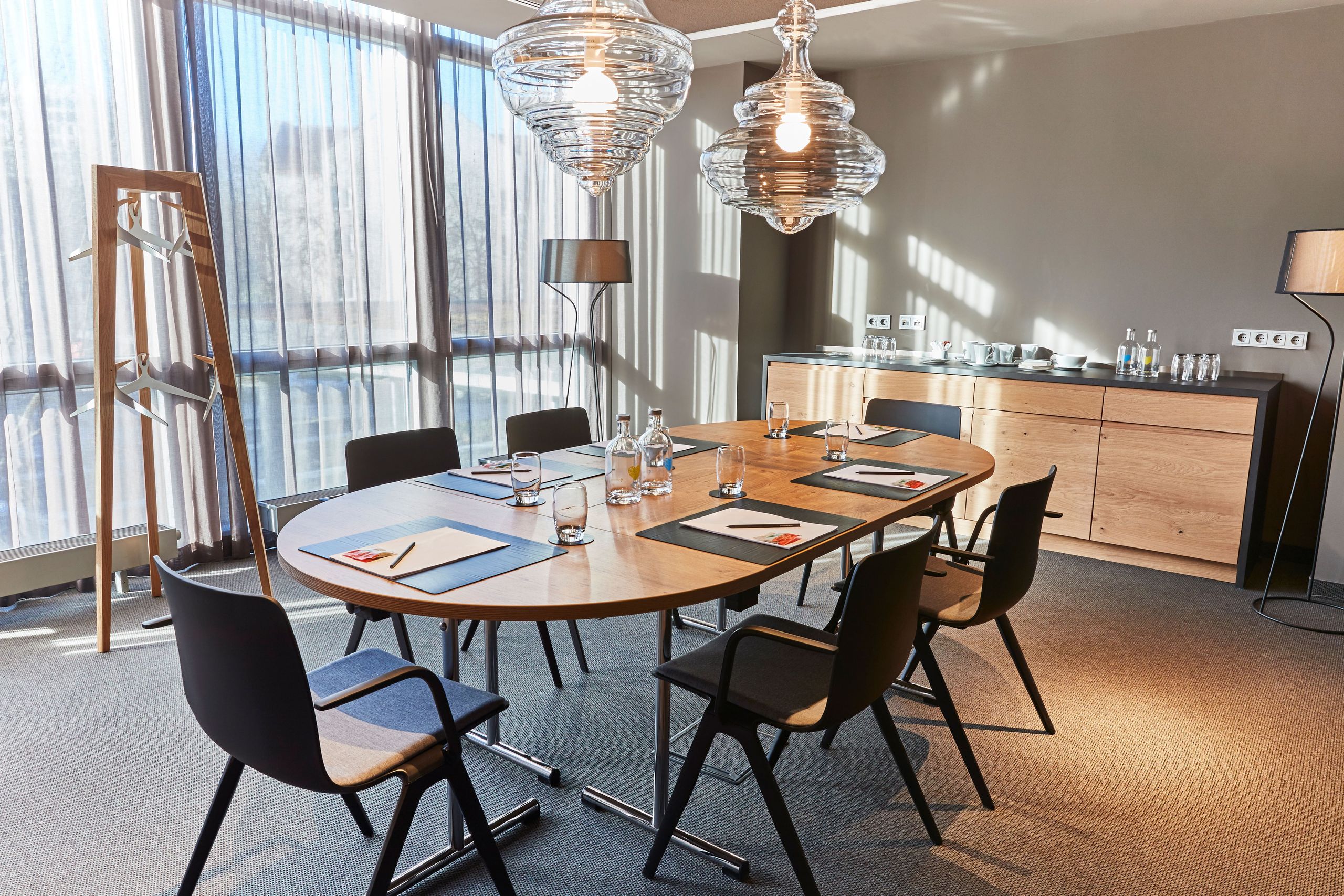 Modern conference room with a long oval table set for a meeting, chairs around it, glass water…