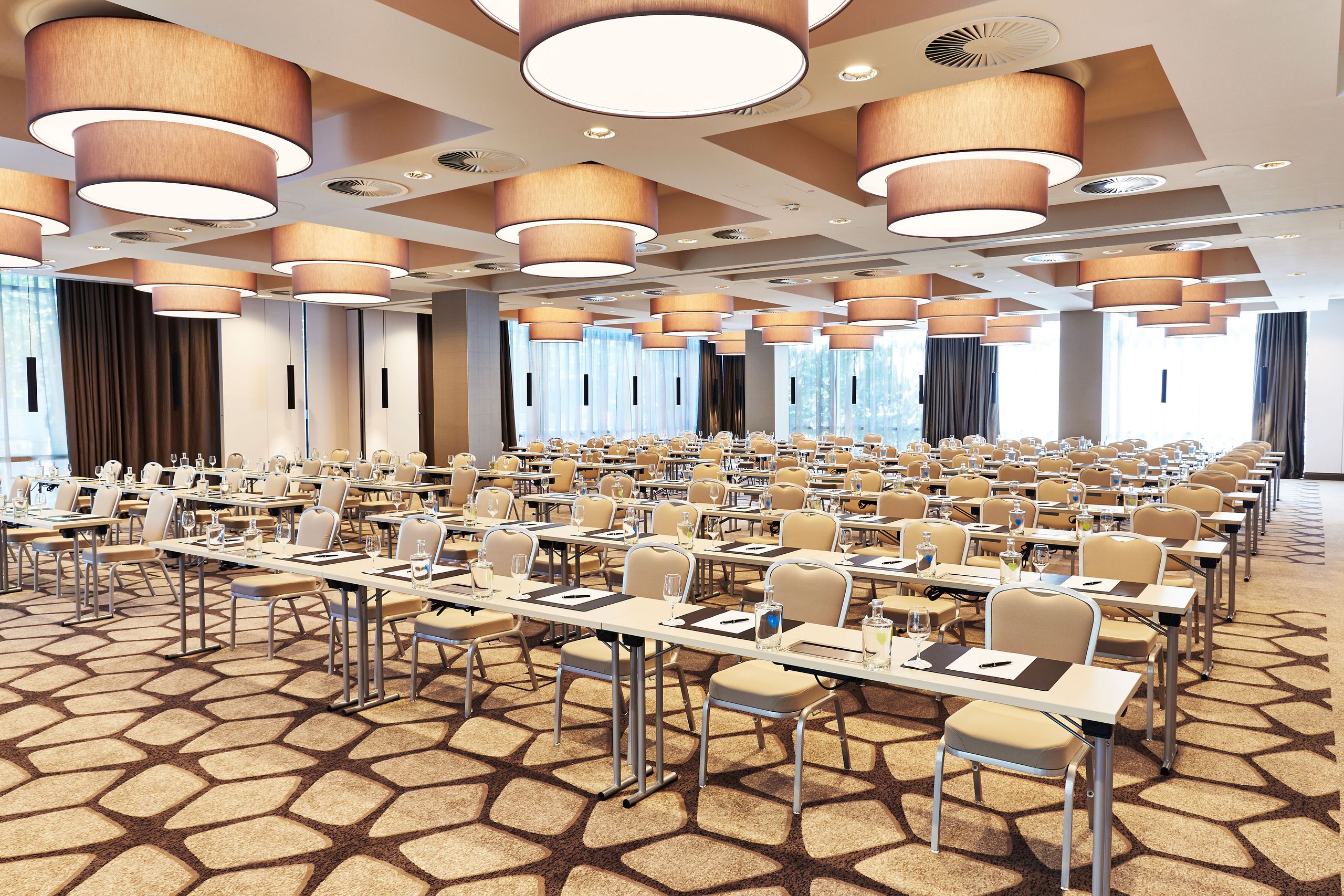 A large conference or meeting room set up with rows of tables and chairs, each table having a…