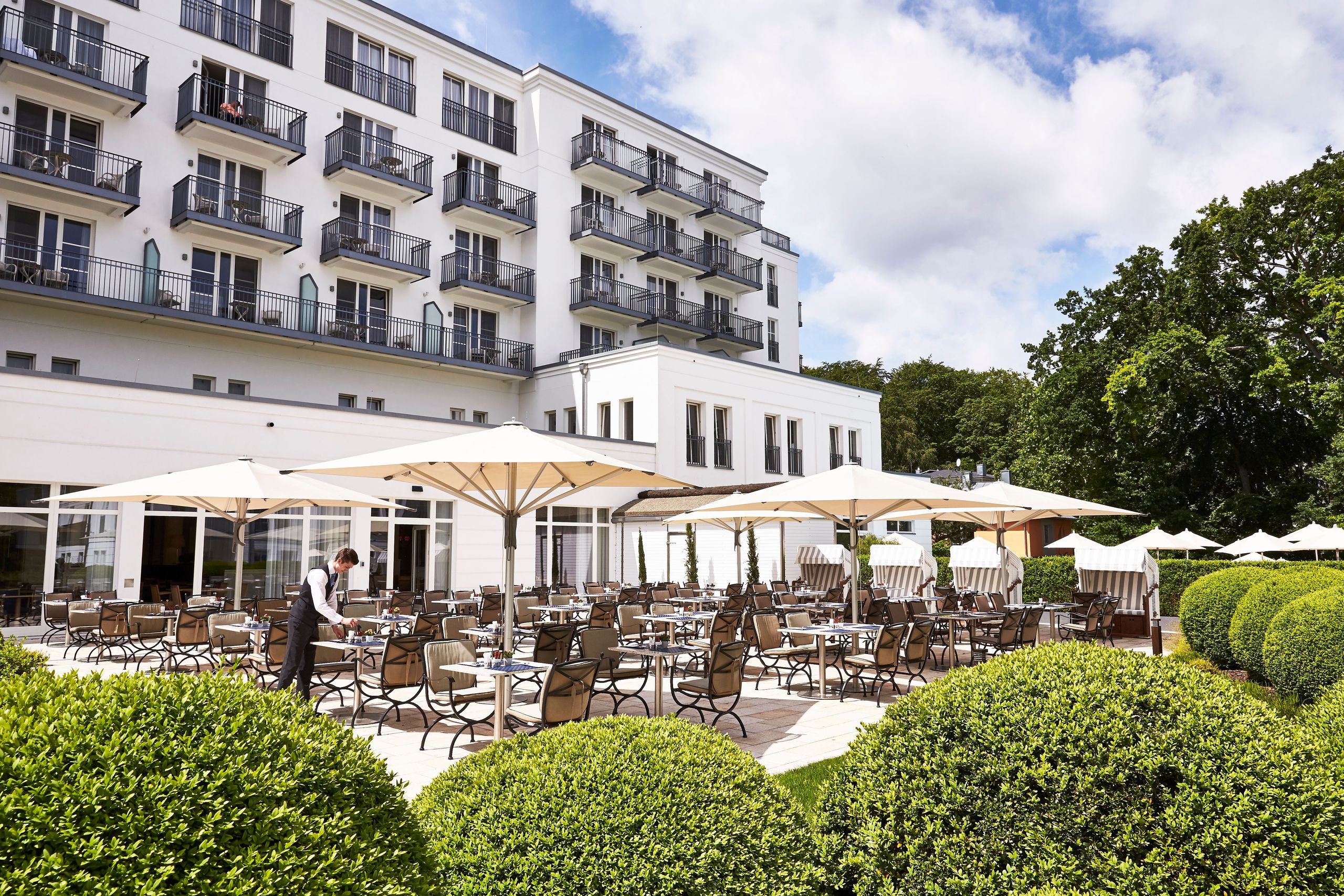 Et udendørs siddeområde ved et hotel eller en restaurant med borde, stole, parasoller og en…