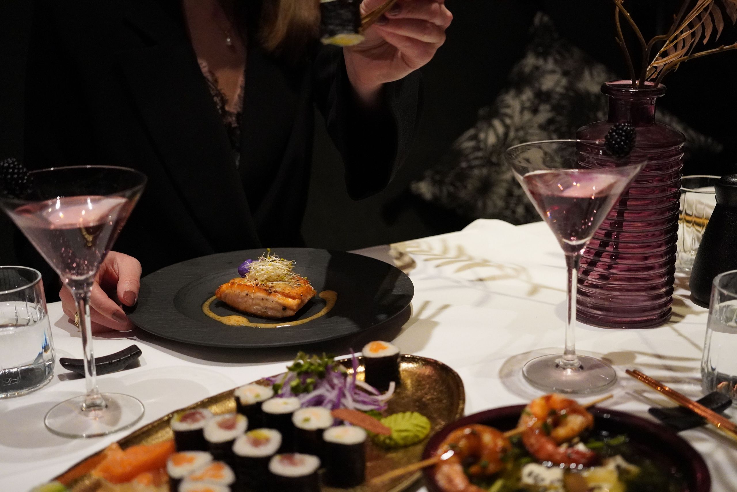 Eine Person isst an einem Tisch mit Sushi, Garnelen und Cocktails.
