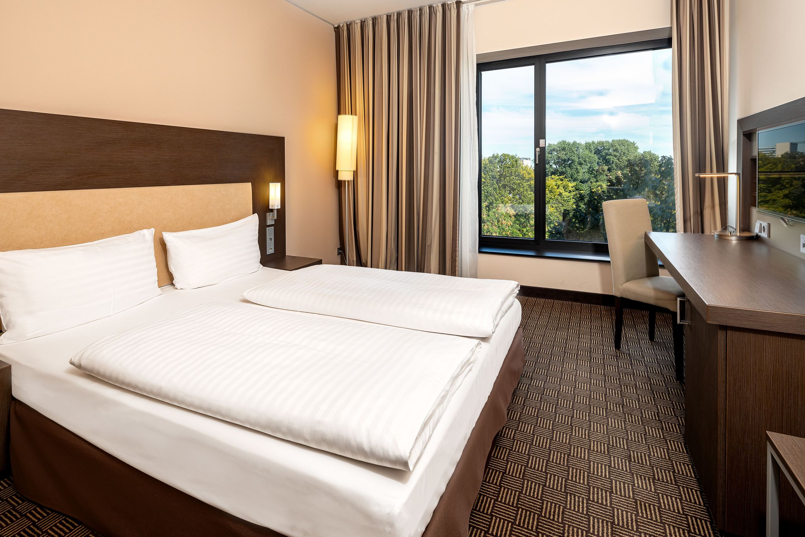 Ein Hotelzimmer mit einem ordentlich gemachten Bett, einem Fenster mit Blick auf Bäume, einem…
