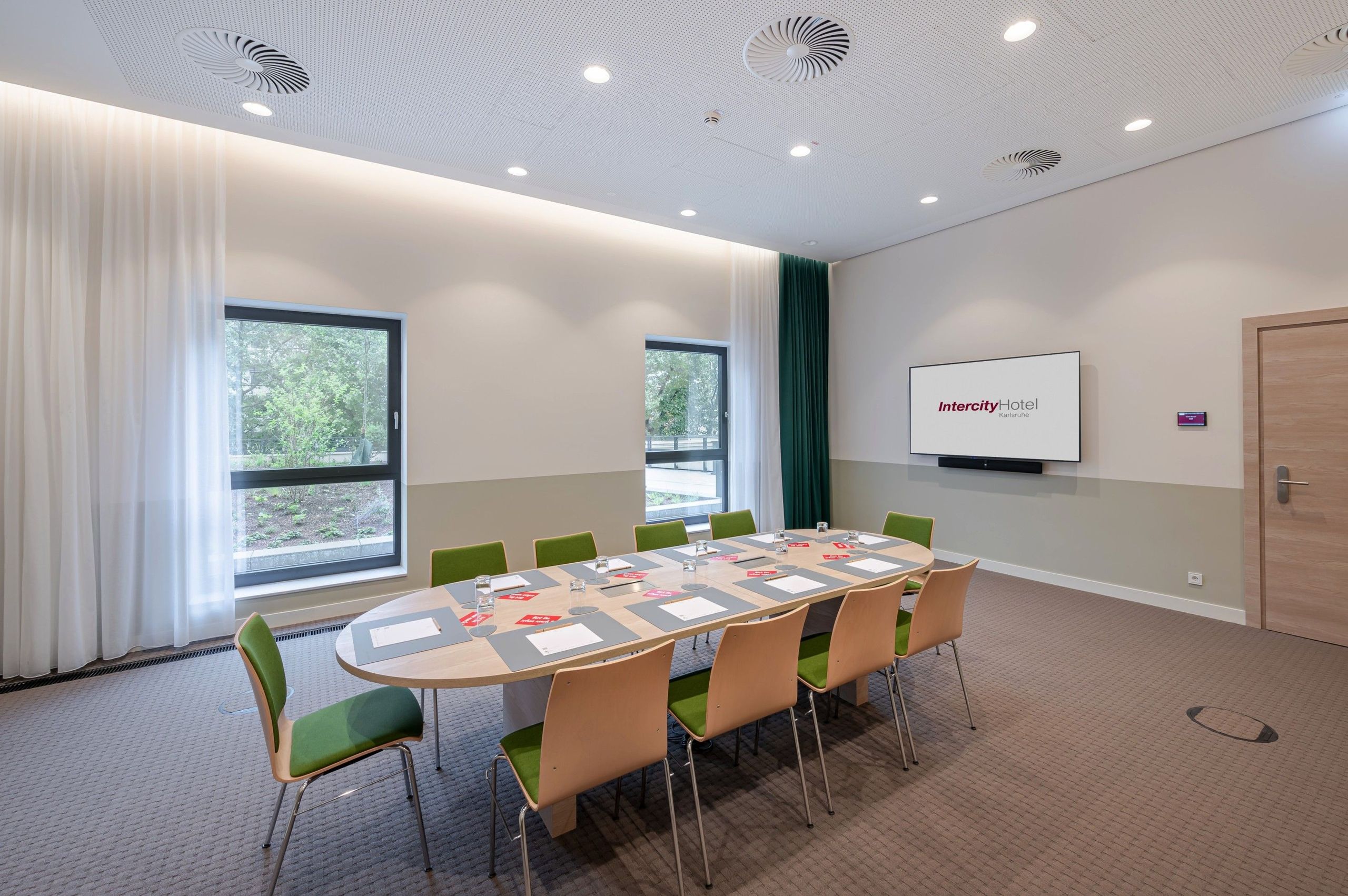 The photo shows a modern conference room with a table surrounded by chairs, some documents on the…