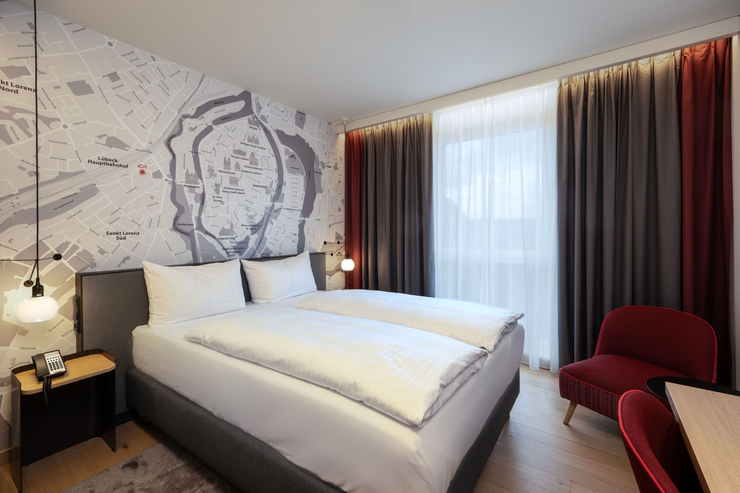 Egy modern hotelszoba franciaággyal, éjjeliszekrényekkel, a falon egy nagy térképpel és függönyös…