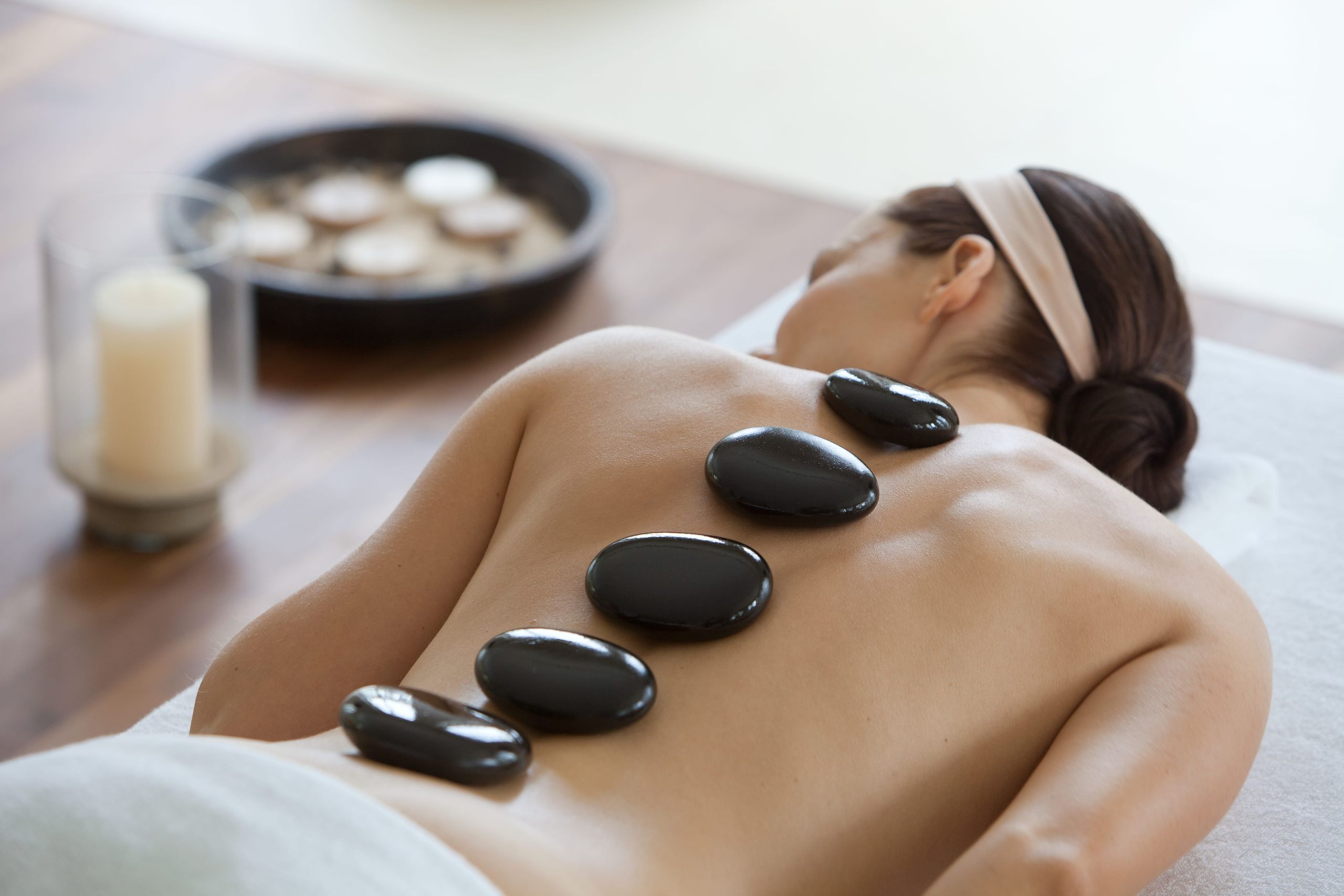 A person receiving a hot stone massage with smooth black stones placed along their back.