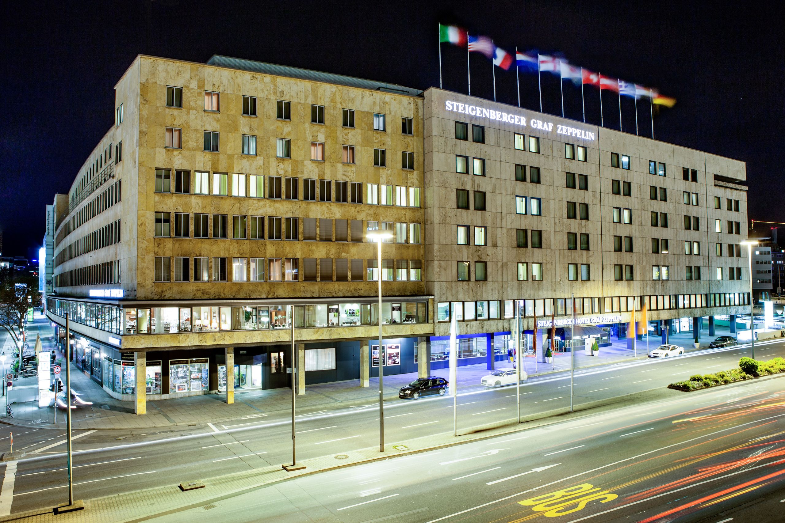 Un edificio grande por la noche con carteles iluminados y varias banderas en el techo.