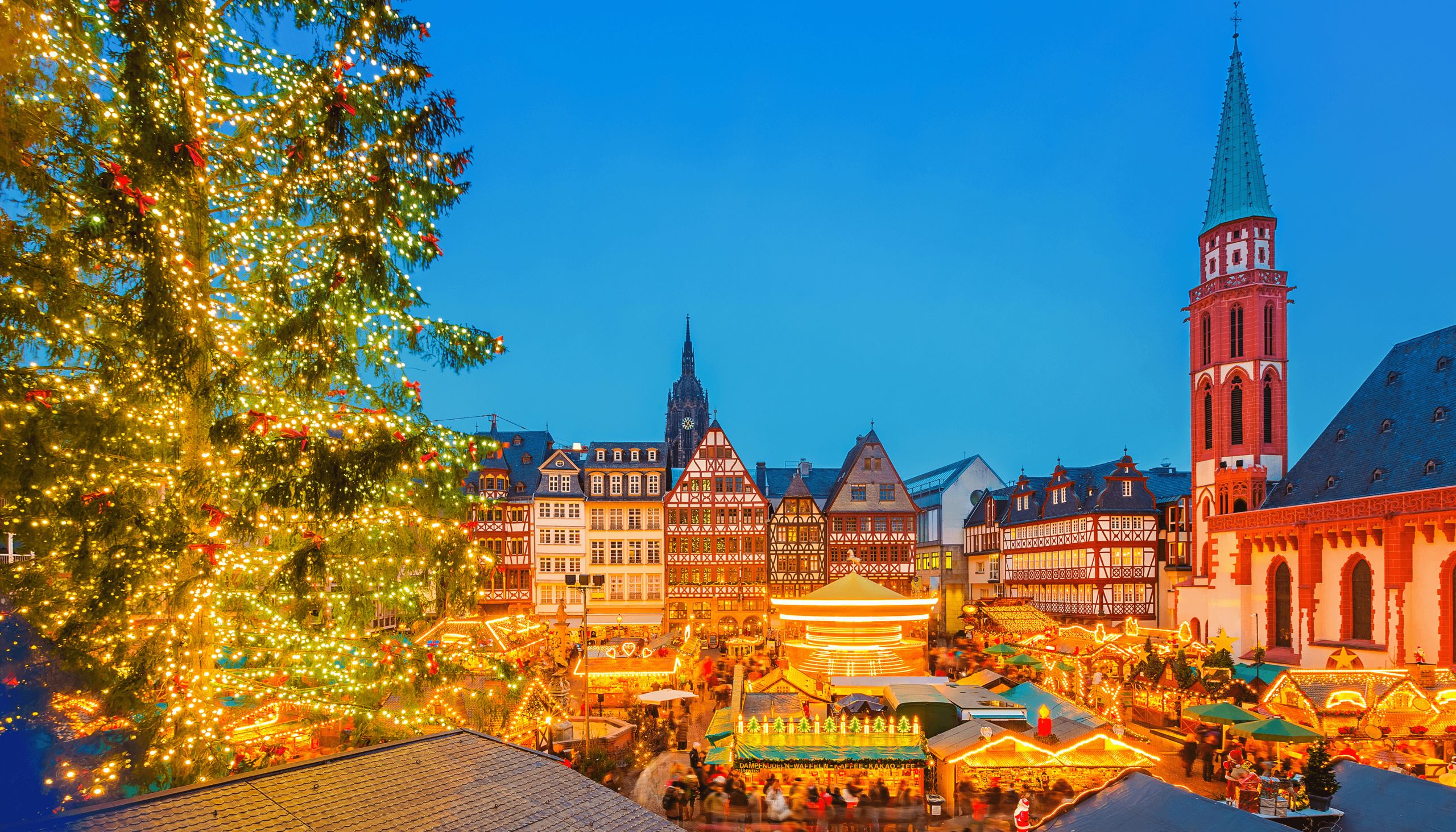 Das Foto zeigt einen festlichen Weihnachtsmarkt mit dekorativen Lichtern, einem großen…