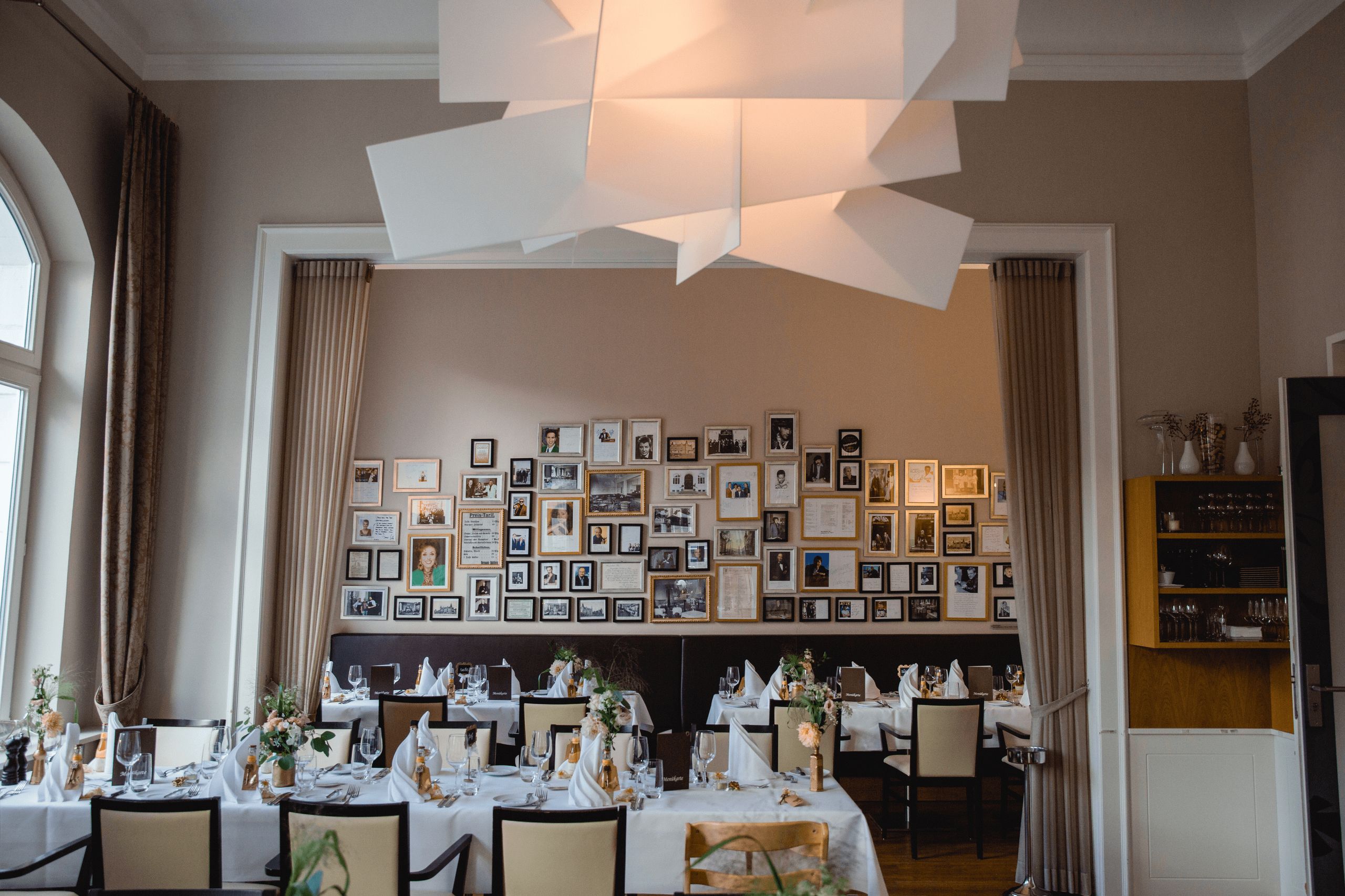 The photo shows an elegantly set dining area with several tables arranged in a row, decorated with…